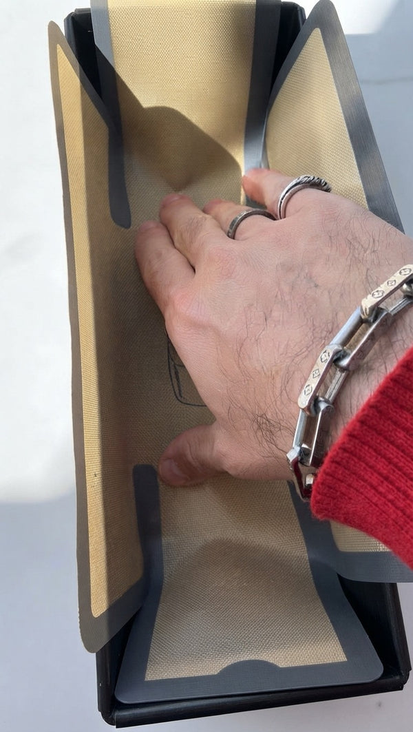 Place your hand inside a specialized baking liner or parchment paper to press and fit it neatly into the base and corners of the dark metal loaf pan.