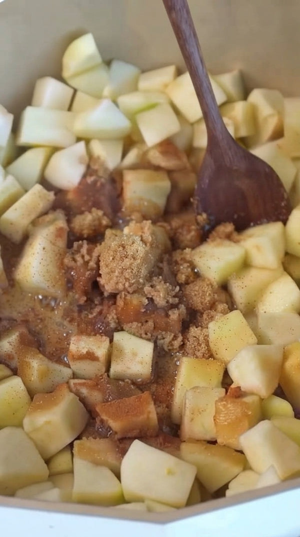 Chop fresh apples into chunks in a pot or bowl, then mix them with brown sugar, cinnamon, and spices using a wooden spoon.