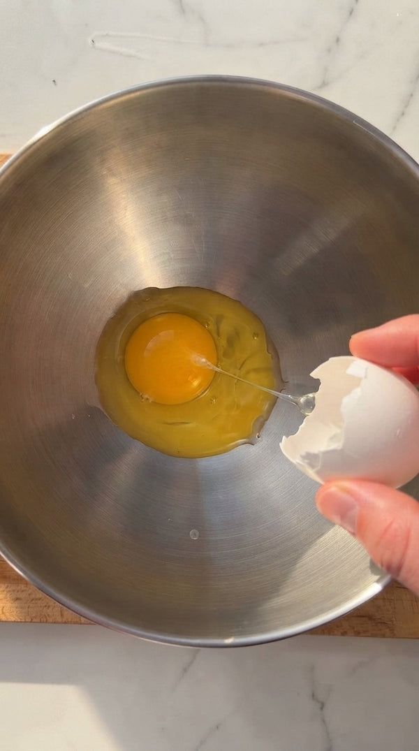 In a separate bowl, the liquid component is prepared. A whisk is used to break an egg into a rich, creamy mixture, creating the base custard or cream layer.