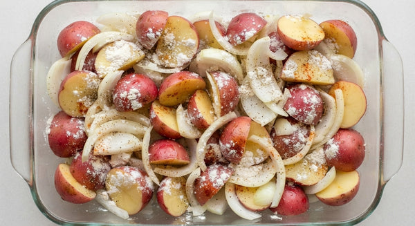 Arrange halved potatoes, onion wedges, garlic, and chicken pieces in a baking dish.