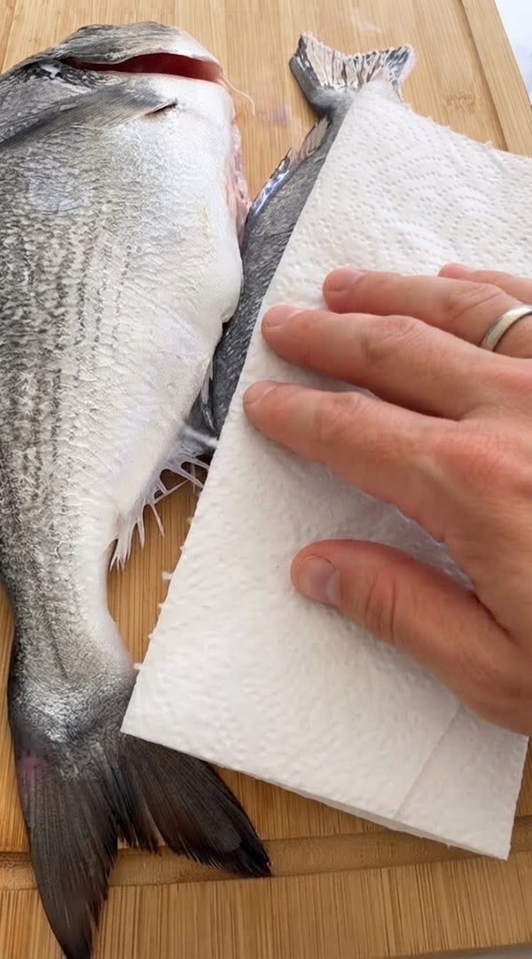 Pat fish completely dry with paper towels. Make 3 diagonal cuts on each side. Rub generously with olive oil, salt, and pepper. Stuff cavity with lemon slices, rosemary, and thyme.