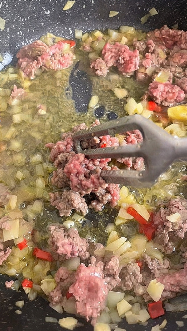 Heat 2 tbsp olive oil in a wide pan. Add diced onions and red peppers, sautéing until translucent. Add ground meat and brown thoroughly, breaking it apart with a spoon.