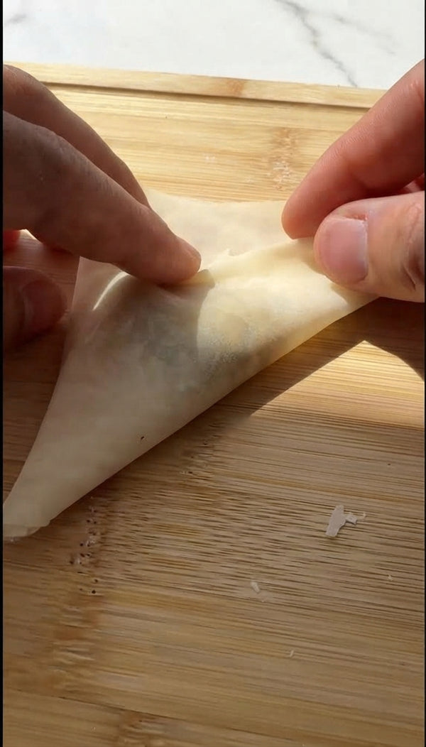 Unroll phyllo dough and cover with a damp towel. Take one sheet, brush lightly with melted butter/oil, and cut lengthwise into long strips (about 7-8 cm wide).